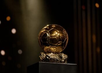 A golden ball-shaped football trophy on a plinth under a spotlight