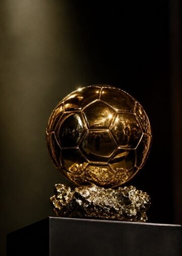 A golden ball-shaped football trophy on a plinth under a spotlight