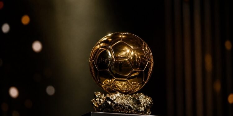 A golden ball-shaped football trophy on a plinth under a spotlight