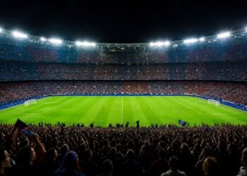 Packed football stadium at night with floodlights and fans in blue and red