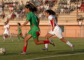 Young female footballers in green and white kits chasing the ball during a match in Morocco