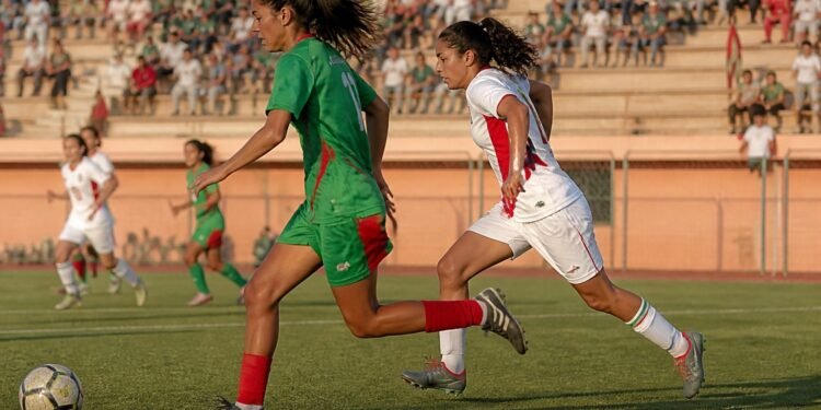 Young female footballers in green and white kits chasing the ball during a match in Morocco