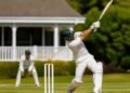 Cricket batsman in green and white kit playing a shot on a green pitch in Nigeria