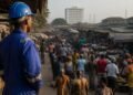 Nigerian worker in overalls standing before a busy market street in morning light
