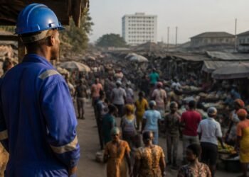 Nigerian worker in overalls standing before a busy market street in morning light