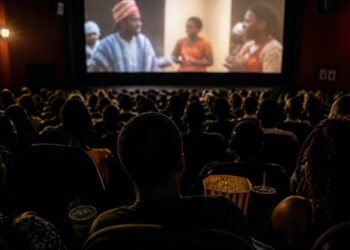Audience silhouettes with popcorn inside a busy Nigerian cinema hall, screen glowing