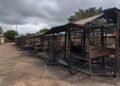 Burned market stalls and debris under an overcast sky in a rural Nigerian town