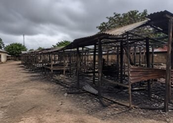 Burned market stalls and debris under an overcast sky in a rural Nigerian town