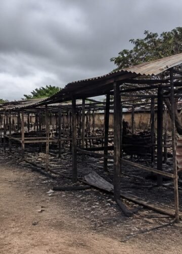 Burned market stalls and debris under an overcast sky in a rural Nigerian town