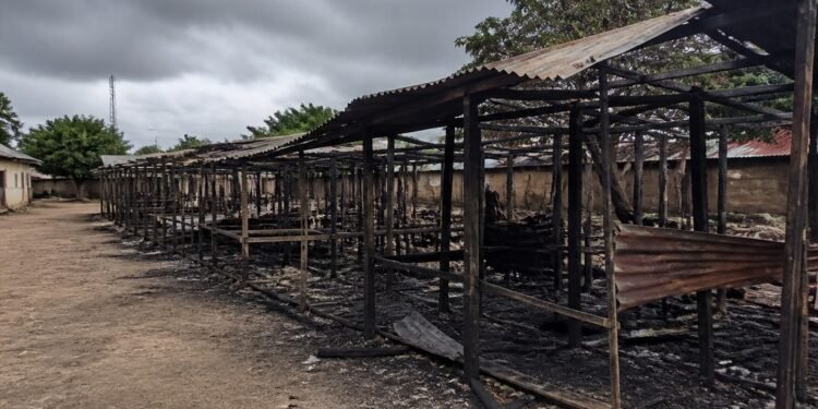 Burned market stalls and debris under an overcast sky in a rural Nigerian town
