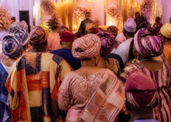 Guests in colourful aso-oke outfits celebrating at a traditional Nigerian wedding venue